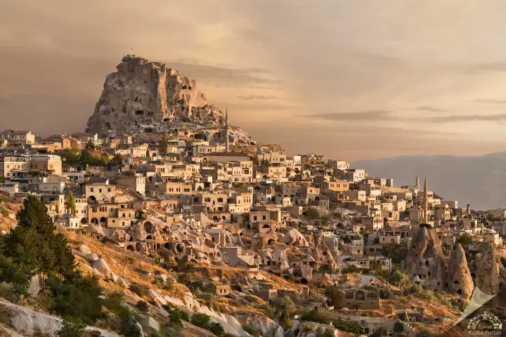 Il Castello di Uçhisar, il punto più alto della Cappadocia, Turchia, domina un panorama dell'ora d'oro sul tessuto urbano circostante di case rupestri e abitazioni scavate nella roccia inondate di calda luce serale.