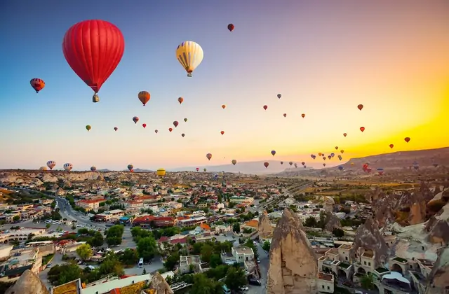 Una singola vivace mongolfiera rossa si libra direttamente sopra mentre un panorama dell'alba si apre su un paese della Cappadocia, Turchia, il suo colore deciso che domina il pallido cielo dorato mattutino.