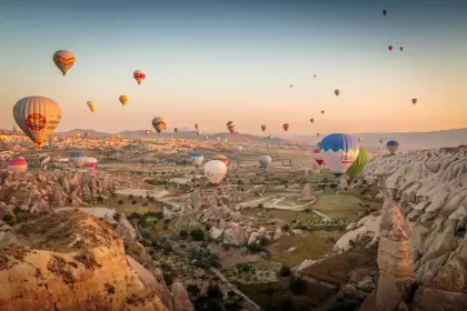 Dozens of hot air balloons fill every corner of the morning sky above the wide open valleys of Cappadocia, Turkey, creating the region's most iconic spectacle of color and flight.