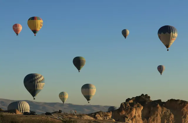 The wide open sky above Cappadocia at sunrise, Turkey, is scattered with hot air balloons at sunrise, their small shapes drifting freely across the immense golden canvas of the morning sky.