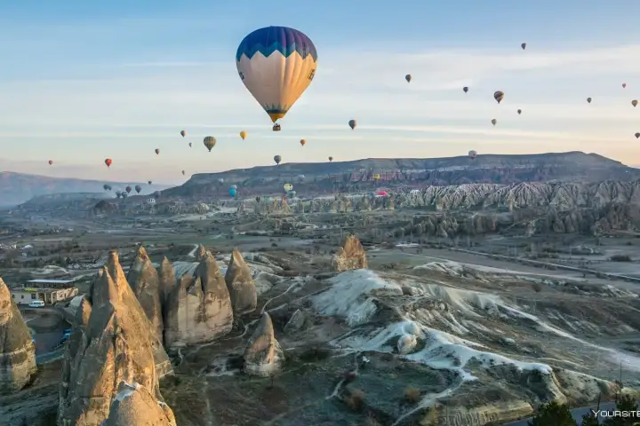 Una mongolfiera gigante domina l'inquadratura in una scena di valle ampia all'alba in Cappadocia, Turchia, il suo enorme involucro che si erge sopra le formazioni rocciose mentre il cielo si schiarisce intorno ad essa.