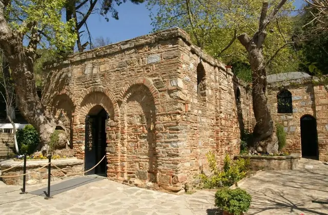 Spring blossoms and fresh green foliage frame the triple-arched stone entrance of the House of the Virgin Mary near Ephesus, Turkey, the Byzantine masonry warm in gentle sunlight on the sacred hillside of Bülbül Dağı above Selçuk.