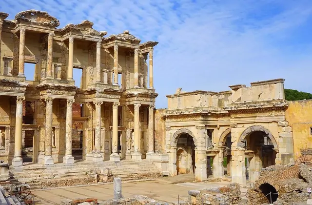 La Biblioteca di Celso e la Porta di Mazeo a Efeso formano un drammatico panorama grandangolare nella pallida luce invernale, con i muri romani adiacenti e l'arcata visibili a sinistra, mentre un cielo giallastro caldo incorona il monumento antico vicino a Selçuk, in Turchia.