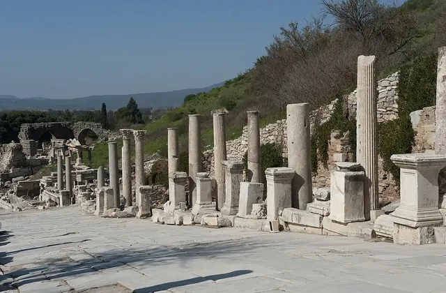 A row of marble columns of varying heights lines the broad paved avenue of Curetes Street at Ephesus, the ancient colonnaded road stretching towards the hillside in clear early-spring light with no visitors present, near Selçuk, İzmir, Turkey.