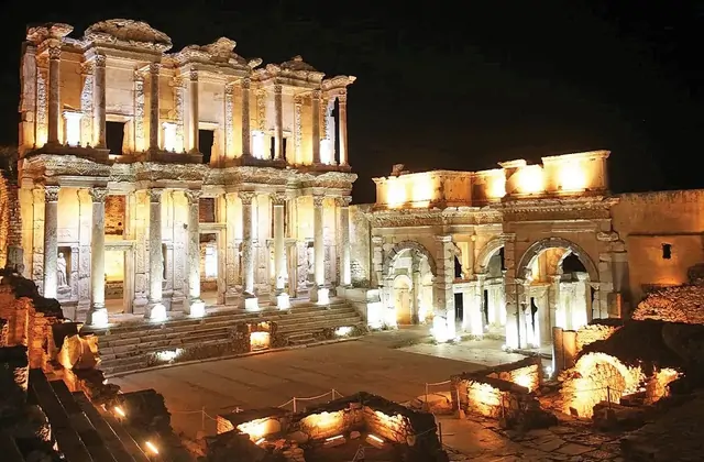 The Library of Celsus and the Gate of Mazaeus at Ephesus shine brilliantly under amber night-time floodlighting, the wide forecourt bathed in soft light against a pitch-black sky in this night-time panorama of the ancient Roman site near Selçuk, Turkey.