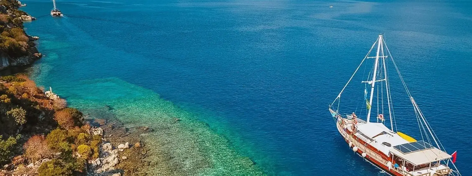 Al tramonto, il porto di Fethiye si trasforma in un tableau dorato dove le silhouette dei velieri e le ombre delle montagne creano un paesaggio da sogno di tranquillità mediterranea.