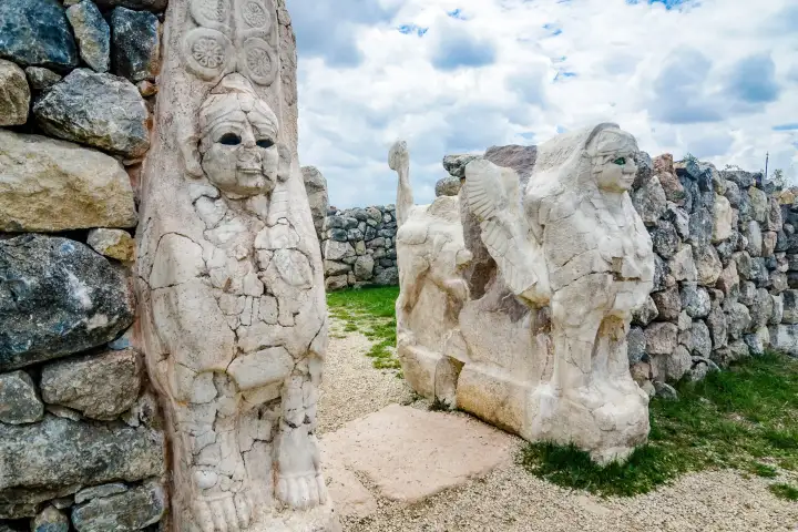 Una vista en ángulo de cerca en la Puerta del Rey, Hattusa, Turquía, muestra la columna guardiana con rostro humano intrincadamente tallada en primer plano, con la esfinge alada y la segunda figura guardiana visibles a través de la abertura de la puerta en la antigua muralla hitita.