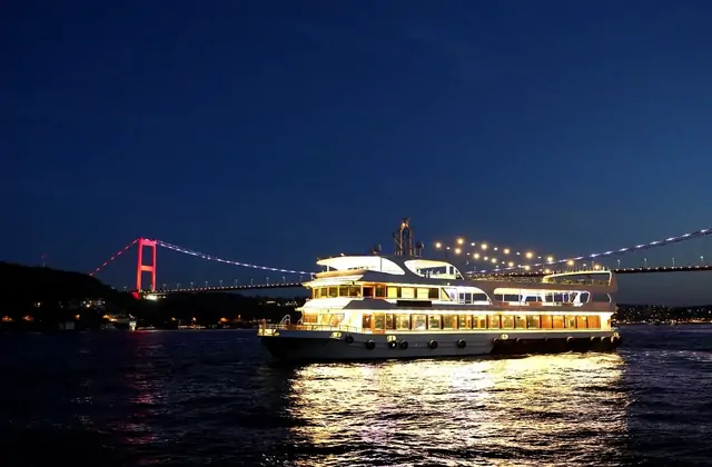 Un battello da cena in crociera sul Bosforo di Istanbul brillantemente illuminato che scivola sullo stretto dopo il tramonto, con i suoi riflessi sull'acqua sullo sfondo dell'iconica skyline della città.