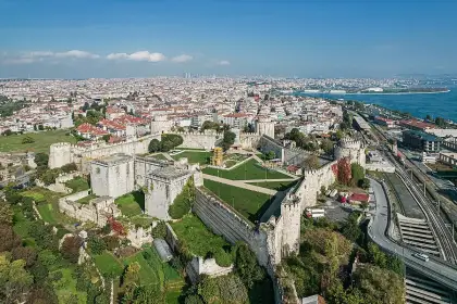 An aerial bird's-eye photograph of Istanbul's ancient Byzantine sea walls shows the fortification complex from directly above, with its massive towers, inner and outer defensive curtain walls and inner green grounds clearly visible, the Bosphorus and Istanbul's dense urban fabric spreading to the ho