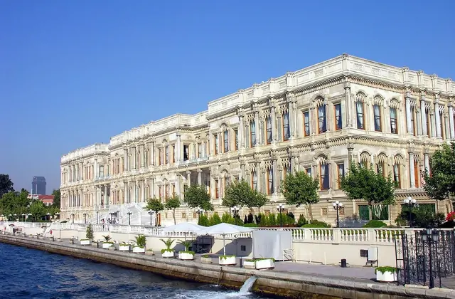Il Palazzo Dolmabahçe a Istanbul fotografato dal Bosforo, la sua facciata lungomare neobaro e neoclassica in calcare bianco lunga 600 metri che si estende lungo l'intera inquadratura con elaborate finestre ad arco su più piani, una terrazza-passeggiata bianca a livello dell'acqua e un limpido cielo