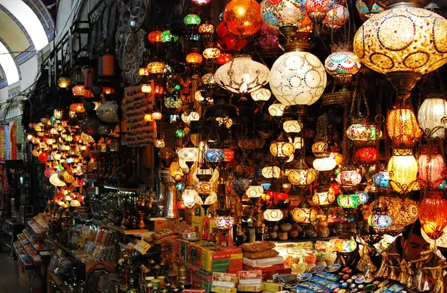 Decine di lanterne a mosaico turco illuminate in ogni colore dello spettro — ambra, cremisi, cobalto, smeraldo e bianco — pendono in fitti grappoli dal soffitto di una bottega di lampade del Gran Bazar di Istanbul, i loro globi in vetro colorato che proiettano riflessi dai toni preziosi sulla merce