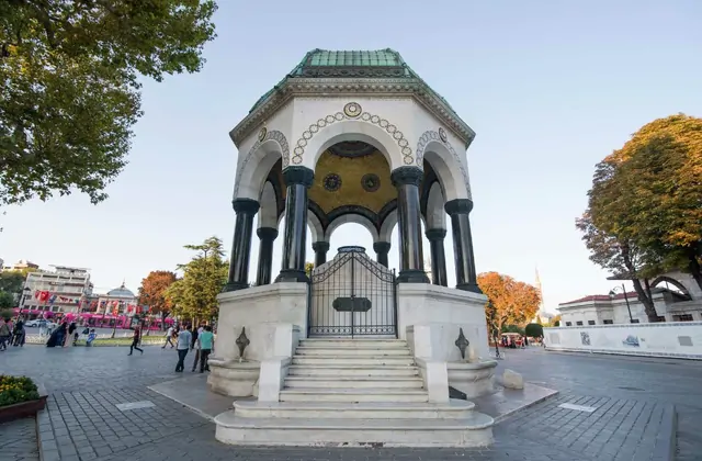 La Fontana Tedesca (Fontana Kaiser Guglielmo II) in Piazza Sultanahmet a Istanbul è fotografata da un angolo basso guardando verso l'alto, la sua struttura neobizantina ottagonale con cupola in rame verde ossidato, soffitto interno a mosaico dorato, colonne in granito scuro lucidato e ornata base in