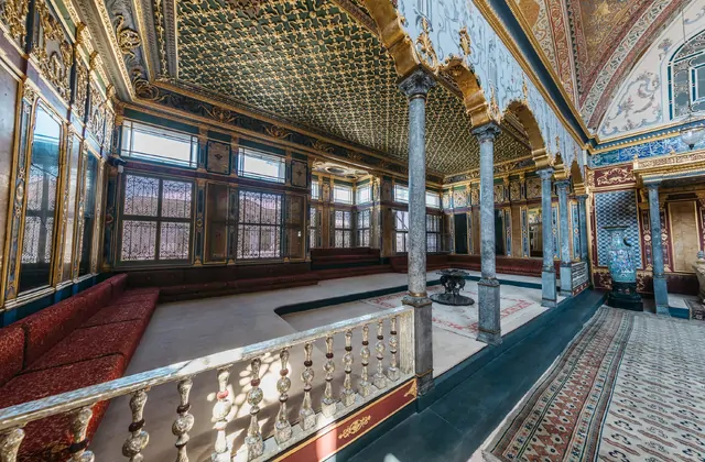 Il lussuoso interno di una camera dell'Harem nel Museo del Palazzo Topkapi di Istanbul visto da un balcone a mezzanino, l'intero soffitto e le pareti superiori coperte da denso mosaico geometrico ottomano verde e oro, con una vasca fontana centrale in basso, colonne di marmo, panche in velluto rosso