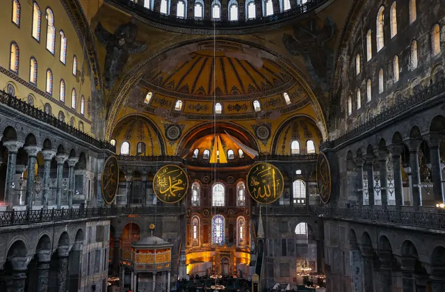 Il vasto interno della Grande Moschea di Hagia Sophia a Istanbul visto dalla navata guardando verso l'abside, l'enorme cupola centrale che si innalza 55 metri sopra la testa e che brilla di caldo oro dall'interno, con grandi medaglioni di calligrafia ottomana che recano i nomi di Allah e del Profeta