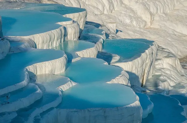 Close-up of Pamukkale's snow-white travertine terraces filled with vivid turquoise thermal water in Turkey, the smooth calcium carbonate rims forming organic semicircles stacked across the entire frame with no sky visible.