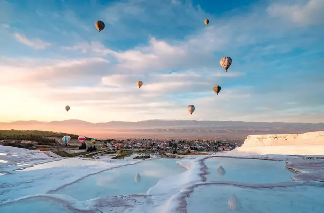 Numerose mongolfiere colorate si levano sulle terrazze di travertino bianco neve di Pamukkale all'alba in Turchia, le piscine poco profonde che riflettono il cielo rosa pallido del mattino.