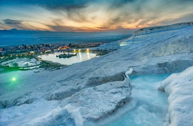 Close view of the Hierapolis theater stage at Pamukkale, Turkey at sunset, the ornate multi-column scaenae frons with carved statues in niches bathed in warm golden light, stone seating rows curving around the orchestra in the foreground.