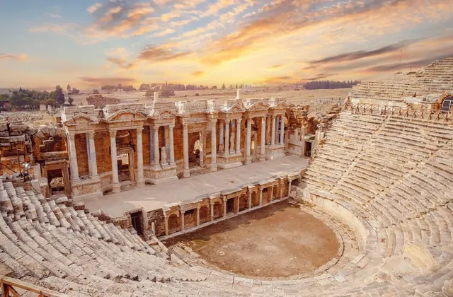 Il teatro di Hierapolis a Pamukkale, Turchia all'ora d'oro con drammatiche nuvole temporalesche che si aprono sopra, fasci di luce che illuminano l'antica facciata del palcoscenico in pietra e le curve file di sedute.