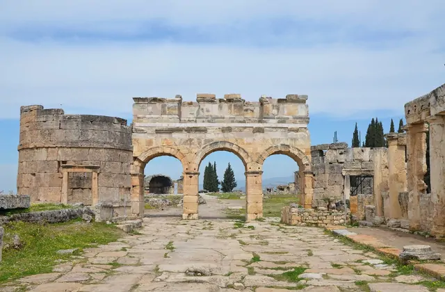 La Puerta de Frontino y la calle porticada de la antigua Hierápolis cerca de Pamukkale, Turquía, una bien conservada puerta de arco de piedra romana enmarcando un camino de adoquines flanqueado por tocones de columnas rotos.