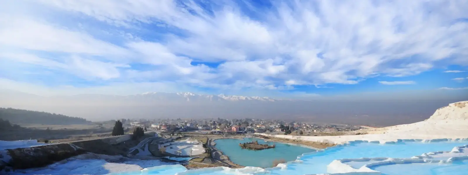 Un sarcófago de piedra cubierto de líquenes sobre soportes de columnas rechonchas yace entre ruinas dispersas en la necrópolis de Hierápolis en Pamukkale, Turquía, un denso bosque al fondo bajo un cielo azul con nubes.