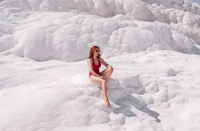 Le terrazze di Pamukkale riprese dal bordo di travertino al tramonto in Turchia, i sinuosi bordi di calcio bianco che brillano di pesca e oro in primo piano mentre le ampie piscine termali blu riflettono il cielo.