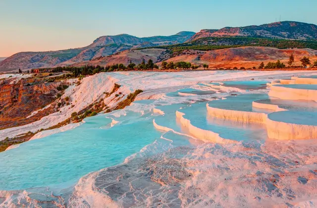 Las terrazas de travertino blanco de Pamukkale al atardecer con suave brillo melocotón y ámbar en Denizli, Turquía, las repisas de calcio en múltiples niveles formando semicírculos de festón llenos de agua turquesa pálida.