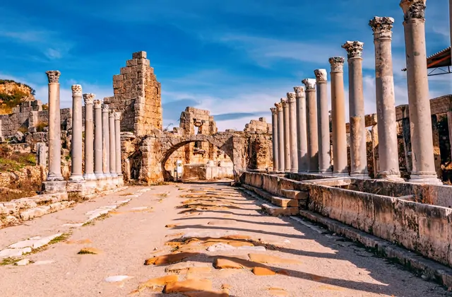 La monumental puerta helenística y las torres redondas que flanquean la entrada a la muralla de la antigua ciudad de Perge, Antalya, Turquía, se elevan sobre el patio abierto pavimentado con piedras antiguas, con sus macizos muros de mampostería con nichos abovedados alzándose contra un cielo azul b
