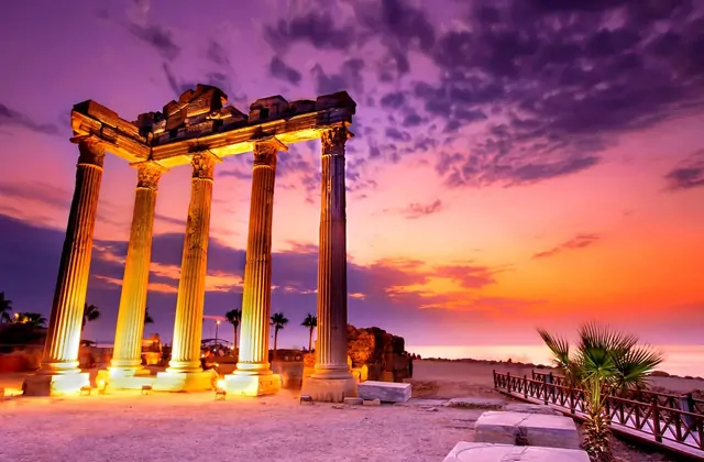 Quattro alte colonne corinzie del Tempio di Apollo a Side, Antalya, sono illuminate in modo drammatico su un cielo al tramonto infuocato nei toni del magenta e del viola, con i loro fusti dorati e la trabeazione parzialmente intatta stagliati sopra la riva del Mediterraneo.