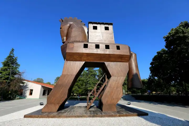 The full-scale wooden Trojan Horse replica at the entrance of the Troy archaeological site in Çanakkale, Turkey, towers over the forecourt in smooth reddish-brown timber, with a rectangular hollow tower body, open windows, and a staircase accessing its belly.