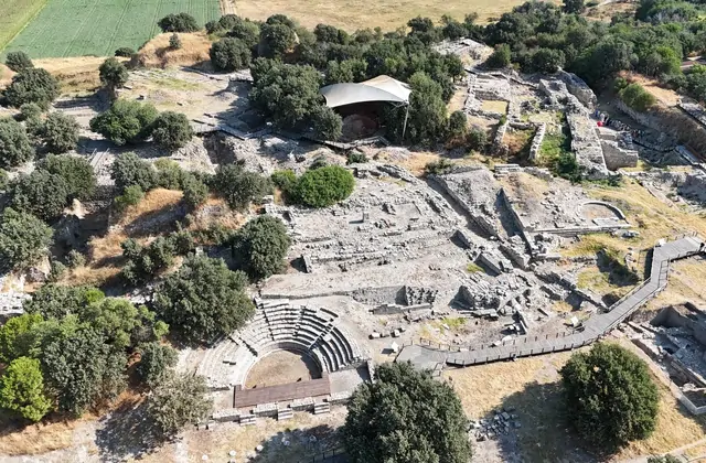Una vista aerea dell'intero sito archeologico di Troia vicino a Çanakkale, Turchia, rivela il teatro odeon semicircolare al margine inferiore, il labirinto di fondamenta di muri in pietra esposti sull'altopiano collinare, una tenda protettiva su un'area centrale di scavo e i circostanti campi coltiv