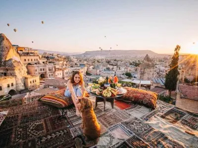Woman enjoying breakfast on a terrace overlooking the fairy chimneys of Cappadocia at sunrise.